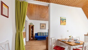 Una habitación con techo de madera, una mesa de comedor con sillas, un sofá azul y una cortina verde.