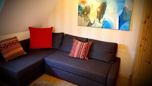 Un canapé modulable avec des coussins à motifs, un grand tableau abstrait accroché au mur et une porte en bois.