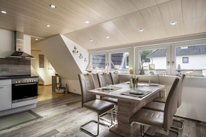 A modern kitchen with a built-in oven, a dining area with a wooden table and chairs, and a staircase leading to an upper level.