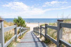 A concrete pathway leading to a beach with a wooden railing on both sides.
