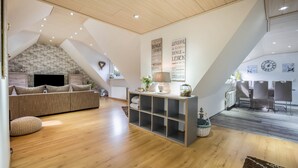 Una sala de estar moderna con un entrepiso, piso de madera, un sofá, un televisor y una estantería.