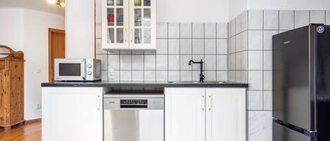 Een moderne keuken met witte kasten, een ingebouwde magnetron, een vaatwasser en een zwarte koelkast.