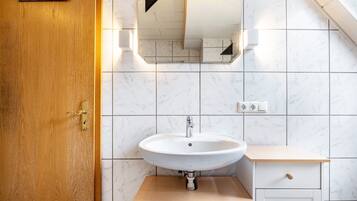 A bathroom with a wooden door, a white sink, a mirror, and a tiled wall.