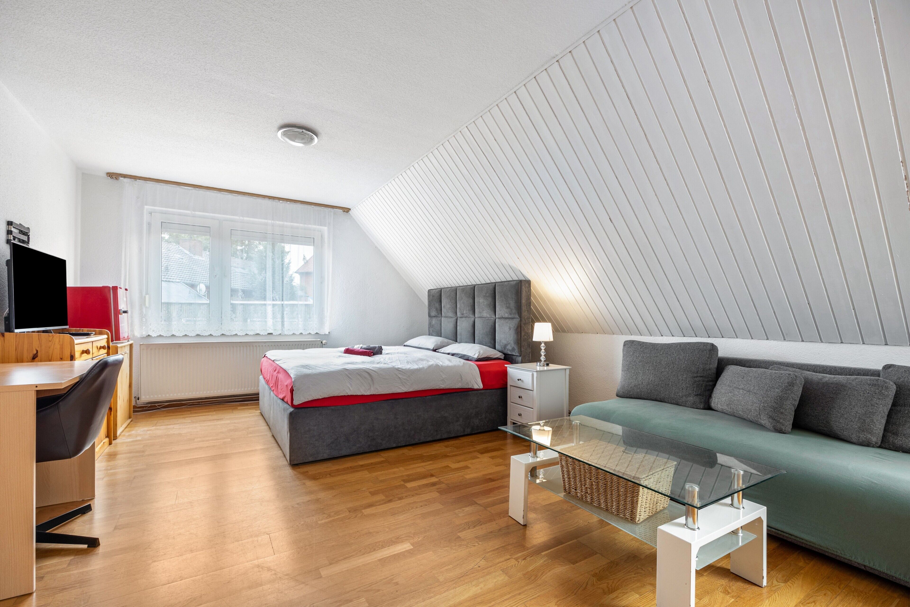 Ein modernes Schlafzimmer mit schrägverdeckter Decke, einem Bett, einem Schreibtisch, einer Couch und einem Glastisch.