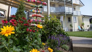 Un edificio con balcón de varios niveles, un jardín de flores variado y un cartel con nombres.