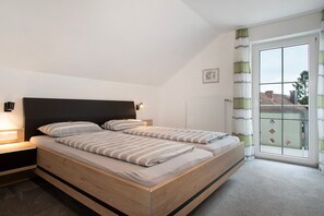A bedroom with a wooden bed, a nightstand, a bedside lamp, and a view through a large window. - Apartment 'Ferienwohnung 2' with Shared Garden, Balcony and Wi-Fi (Wasserburg (Bodensee))