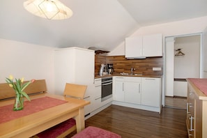 Una cocina compacta con armarios blancos, encimera de madera y una zona de comedor con mesa y sillas.