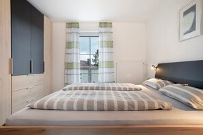 Un dormitorio con cama, cortinas, cabecero, ventana y radiador.
