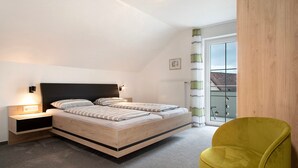 Quarto com cama, mesas de cabeceira, uma cadeira e janela com vista.
