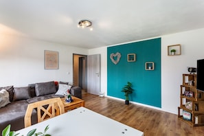 Een woonkamer met een bank, salontafel, turquoise accentmuur en een tv-meubel.
