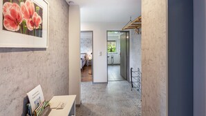 Un pasillo con una obra de arte floral enmarcada, una mesa de recepción con un cartel, un perchero y una vista de un baño con ducha.