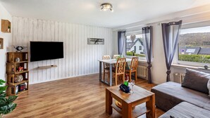 Una sala de estar con televisor de pantalla plana, muebles de madera, una mesa de comedor y un sofá.