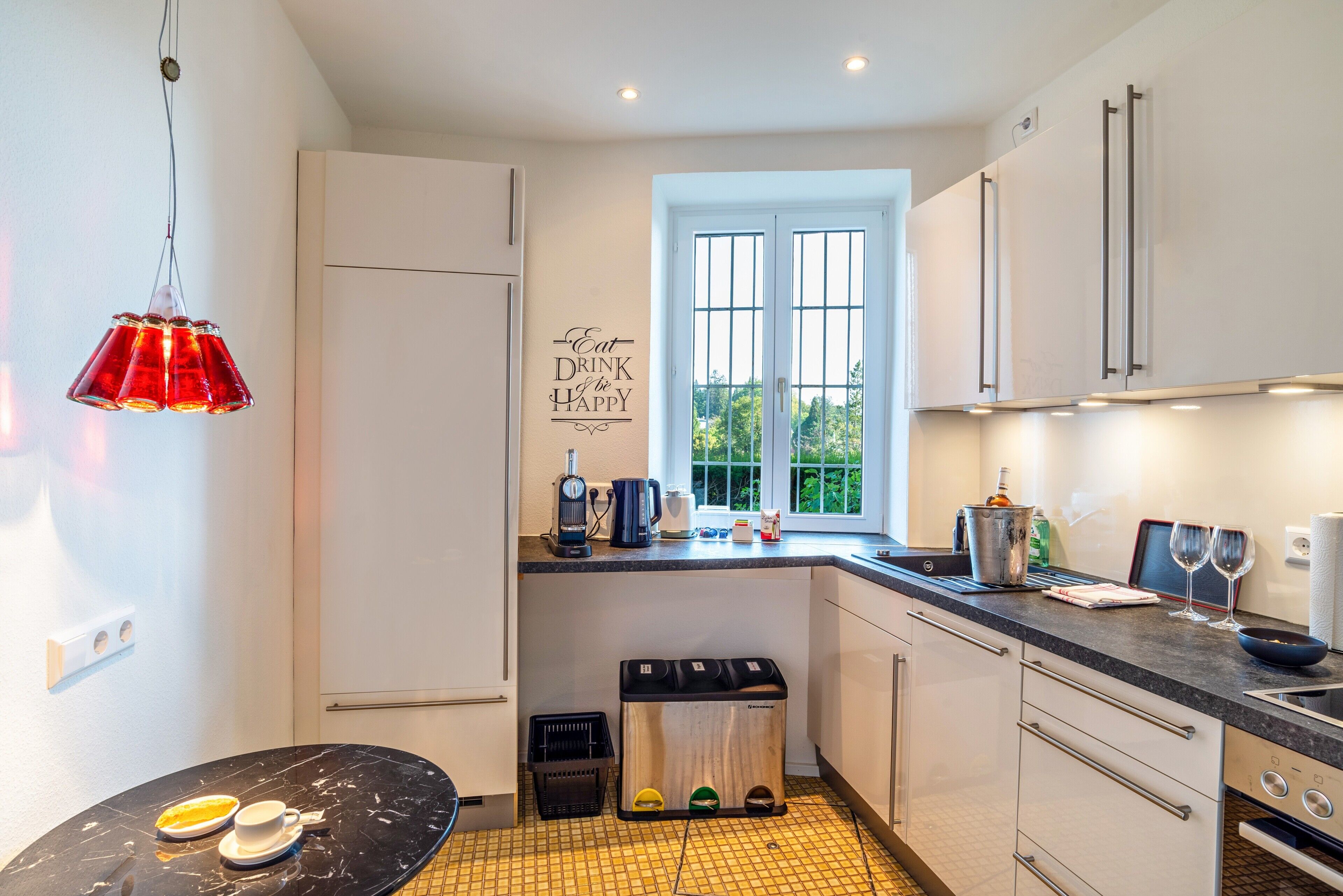 A modern kitchen with a black countertop, white cabinets, a window, and a red pendant light.