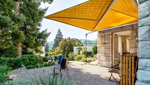A covered outdoor seating area with a gravel floor, surrounded by greenery and a stone wall. - Holiday Apartment "Merkurblick" with Mountain View & Private Terrace, WLAN (Baden-Baden)