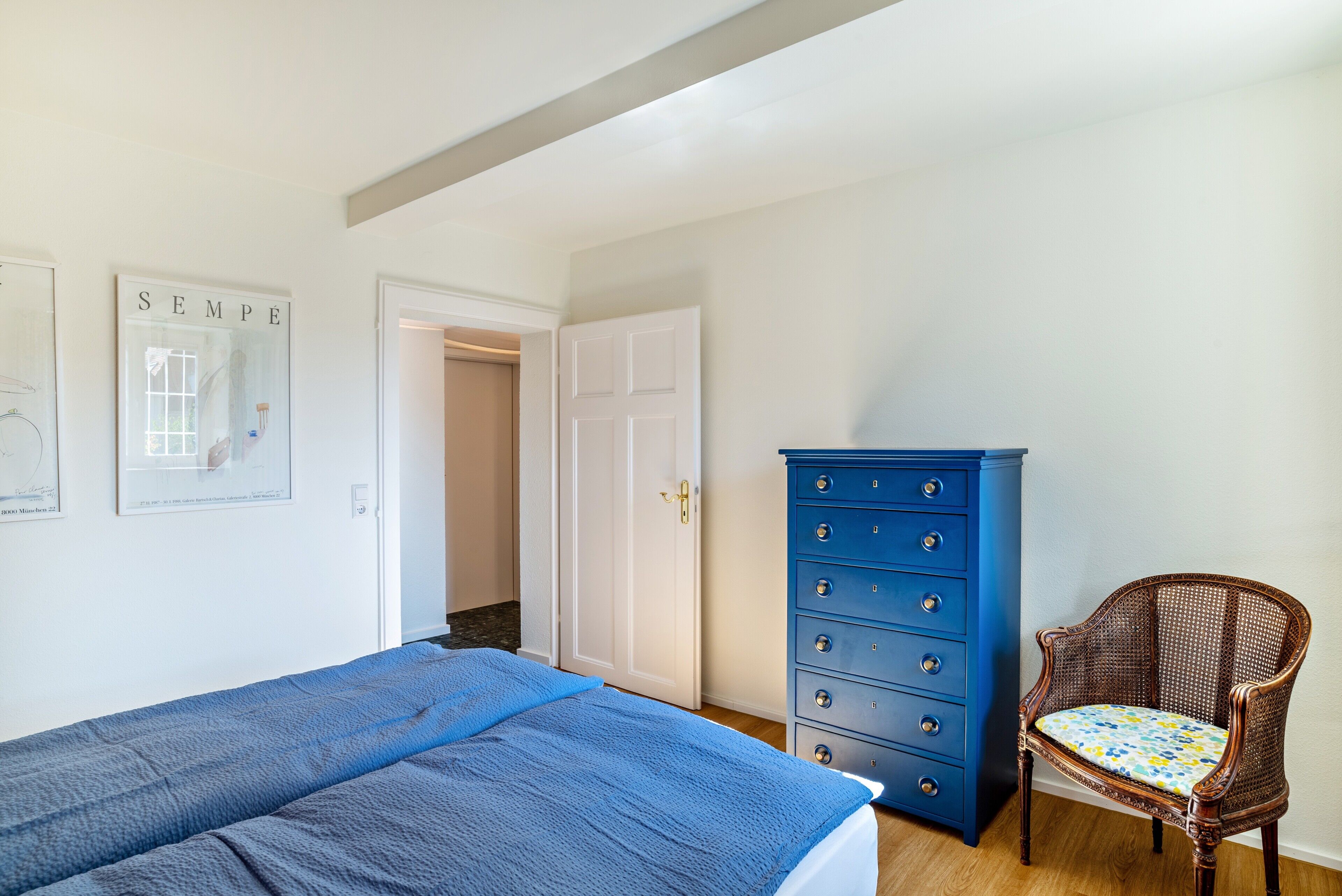 Ein Schlafzimmer mit einem Bett, einem Schminktisch, einem Sessel und einer Tür zu einem anderen Raum.