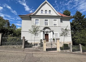 A two-story building with a symmetrical facade, a central entrance with a wooden door, and a red-tiled roof.