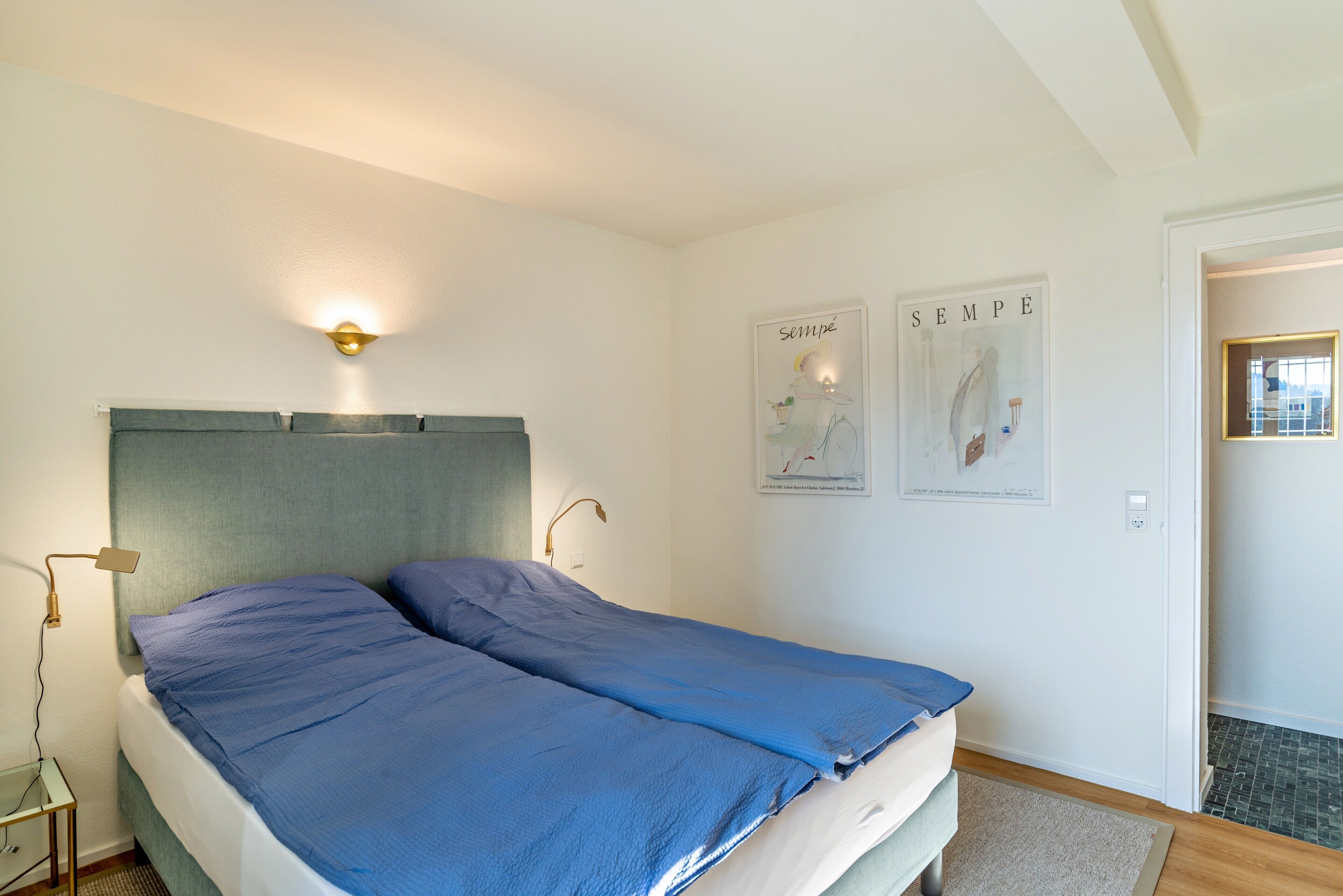 A bedroom with a bed, bedside lamps, a wall-mounted light, and two posters.