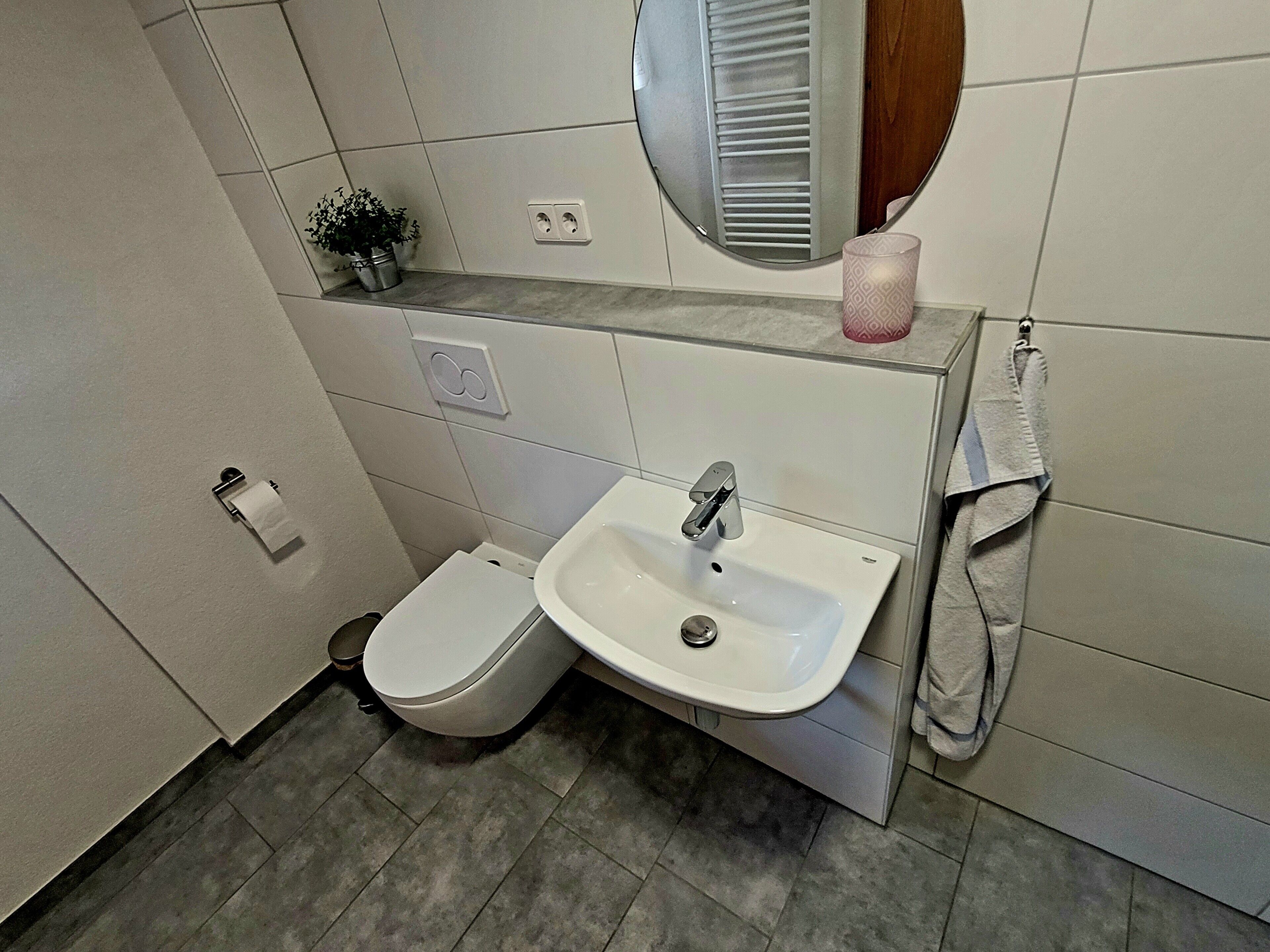 Ein Badezimmer mit Toilette, Waschbecken, Spiegel, Handtuchhalter und einem kleinen Topfpflanzen.