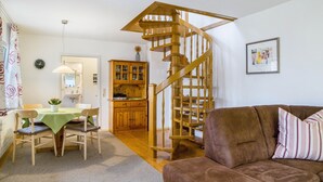Una sala de estar con un sofá marrón, un comedor con mesa y sillas, una escalera de madera y una cocina con armarios de madera.