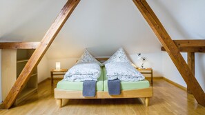 Une chambre à coucher aménagée dans un espace de type « loft », avec un plafond en bois, un lit avec une literie verte, deux tables de chevet et une petite table de nuit avec une lampe.
