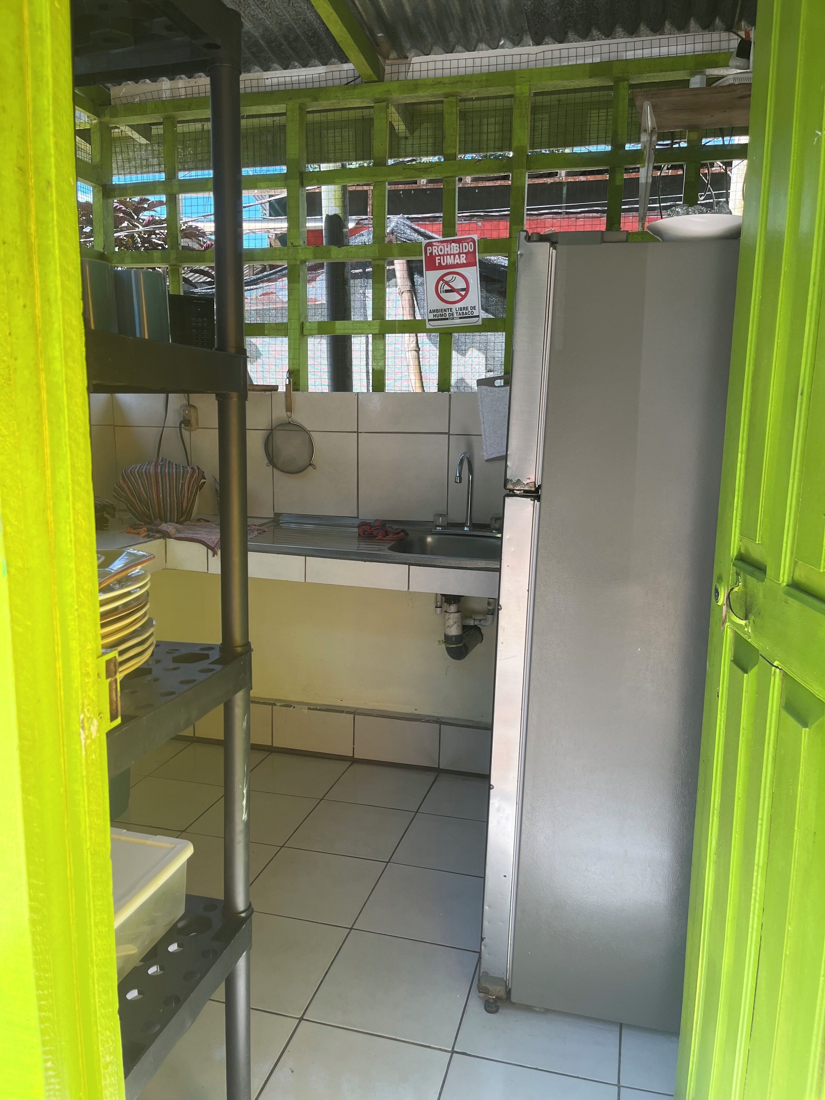 Una pequeña cocina con refrigerador, lavamanos y piso de baldosas.
