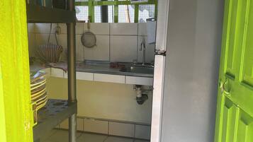 Una pequeña cocina con refrigerador, lavamanos y piso de baldosas.