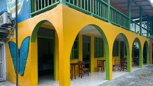 Un edificio con paredes amarillas y arcos verdes, que presenta un mural de mariposas y asientos al aire libre.