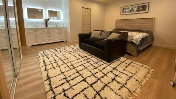 A bedroom with a bed, a sofa, a large rug, a headboard, a mirror, and a door.