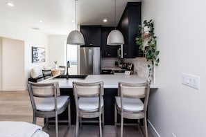 A modern kitchen with a central island, two pendant lights, and a dining area with three chairs.
