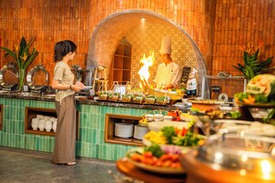 Montaje de bufé con un chef cocinando al fondo, rodeado de diferentes alimentos y utensilios de bufé.