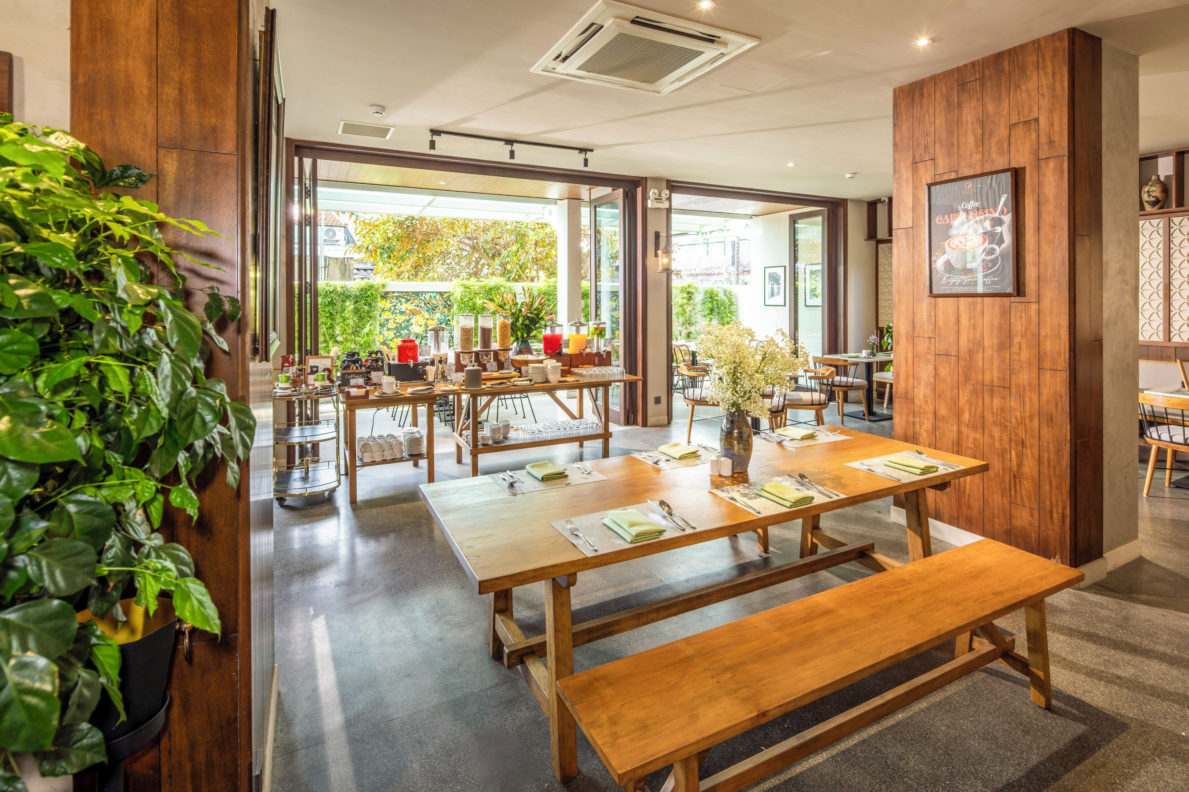 A café with wooden tables and benches, a coffee station, and a view of the outdoors.