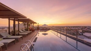 Eine Dachterrasse mit Liegestühlen und einem Pool mit Blick auf eine Stadtlandschaft bei Sonnenuntergang.