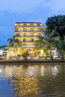 Un hotel de varios pisos con balcones, vista al agua, mesas al aire libre y un letrero que dice 'VITILECEM HOTEL'.
