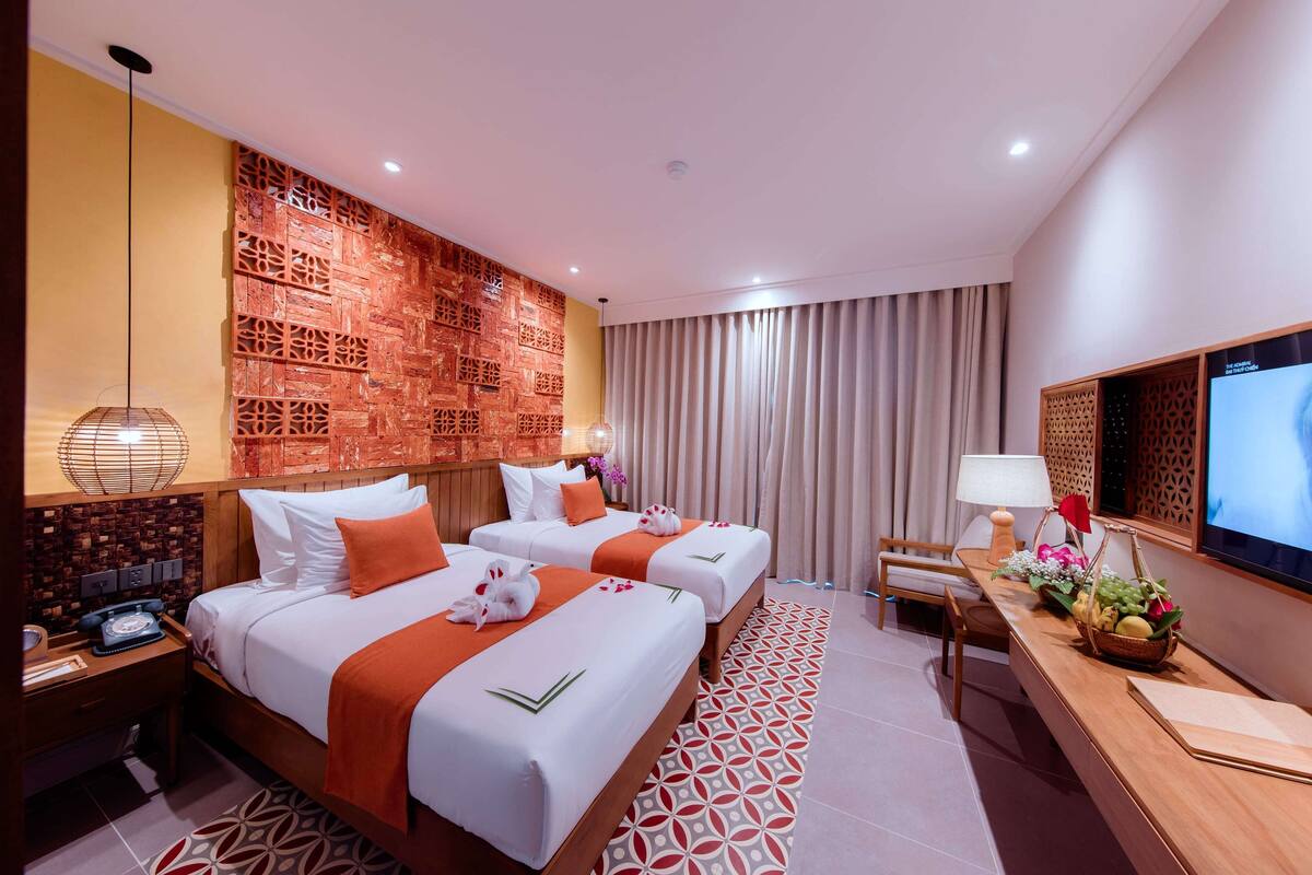 A hotel room with two beds, a desk with a TV, a decorative wall, and a patterned rug.