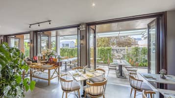 A spacious dining area with multiple tables and chairs, large windows offering views of the outdoors, and a modern interior design.