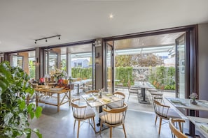 Un amplio comedor con múltiples mesas y sillas, ventanas grandes que ofrecen vistas al exterior, y una decoración de diseño moderno.