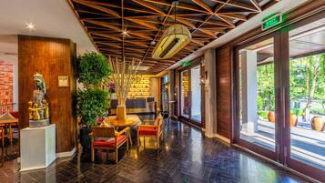 A hotel lobby with a modern design, featuring a wooden ceiling, a reception desk, and a seating area with chairs and a table.
