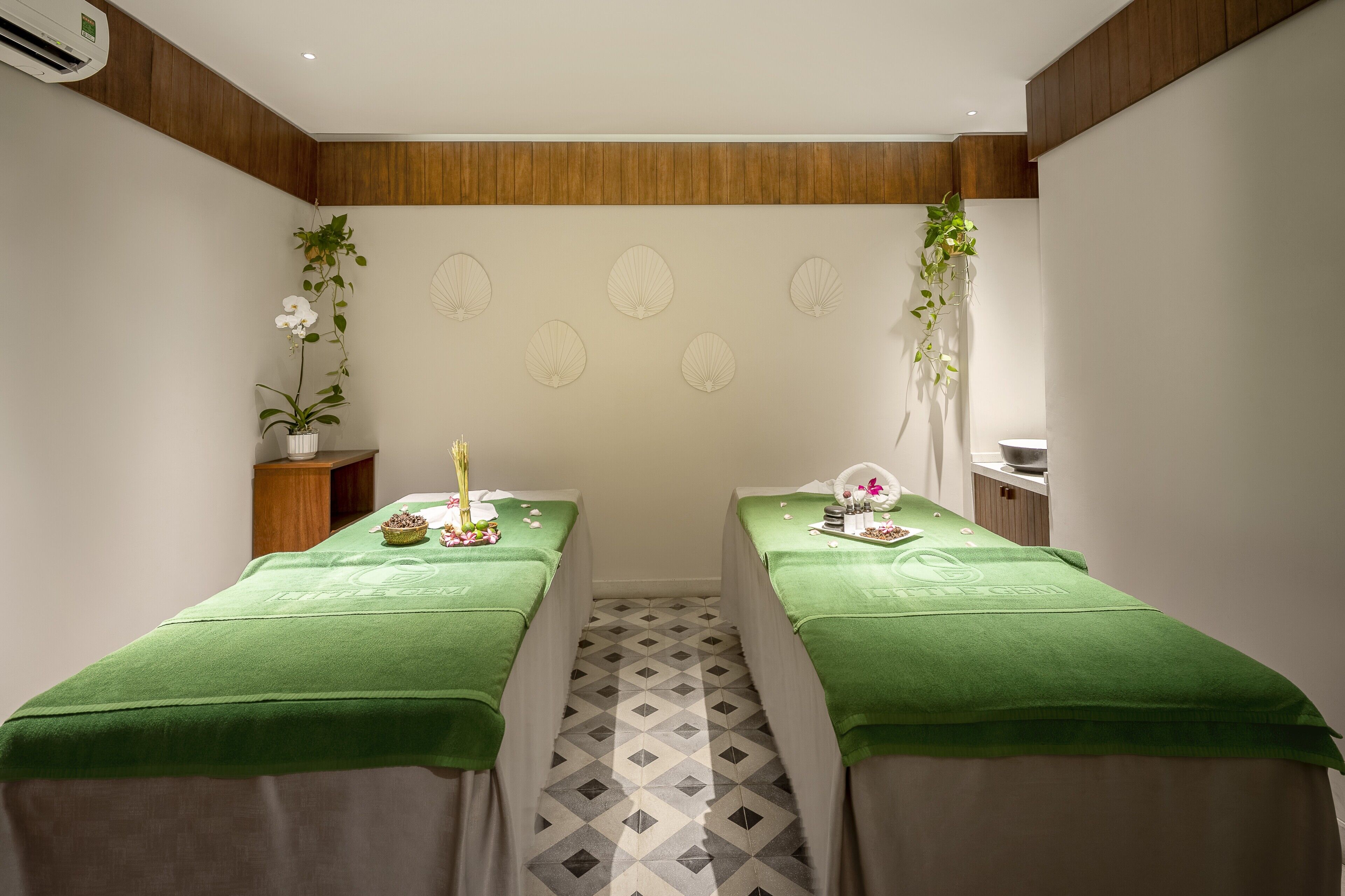 A spa room with two treatment tables, each covered with a green towel, and a wooden panel wall with decorative wall art.