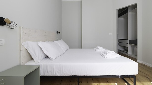 A modern bedroom with a white bed, neatly folded white towels, and a wooden headboard. - Italianway Collection - Stradivari 4 (Milan)