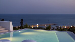 An infinity pool with a view of the ocean and a pier in the background.