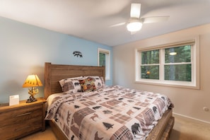 A bedroom with a bed, nightstand, lamp, and a window with a forest view.