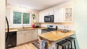 A modern kitchen with white cabinets, a granite countertop, a built-in microwave, and a window overlooking a forest. - Spacious Home near Diana's Baths! (Conway)