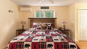 A bedroom with a bed featuring a quilt with animal prints, a ceiling fan, a window with a view of trees, and a door to the right. - Spacious Home near Diana's Baths! (Conway)