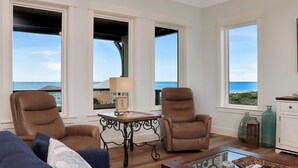 A living room with two leather chairs, a glass coffee table, and a view of the ocean through large windows. - The Sea Life (Port St. Joe)