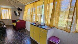 Een knus woongedeelte met een kitchenette, een bank, een rode stoel en een aan de muur bevestigde televisie.