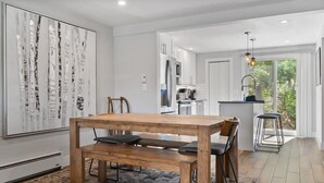 Una cocina moderna con armarios blancos, una mesa de comedor de madera con bancos y vistas al exterior a través de un ventanal grande.