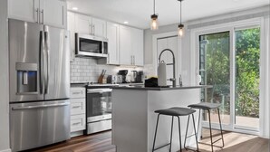 Una cocina moderna con electrodomésticos de acero inoxidable, una isla central con taburetes y un amplio ventanal corredero a una terraza.