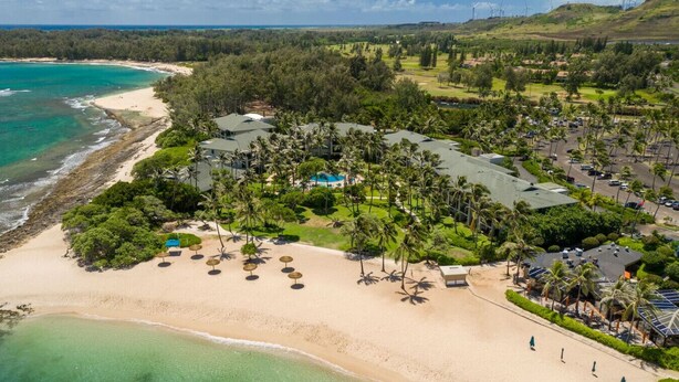 Luchtbeeld van een resort met een strand, palmbomen en een golfbaan op de achtergrond.