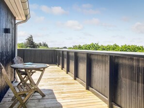 Eine Holzterrasse mit Tisch und Stühlen, Blick ins Grüne und ein klarer Himmel.