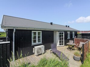 Ein schwarzes Haus mit einer Terrasse, einer weißen Tür und einem Fenster.